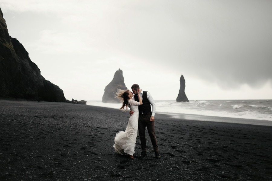 Couple embracing on a black sand beach beneath sea stacks