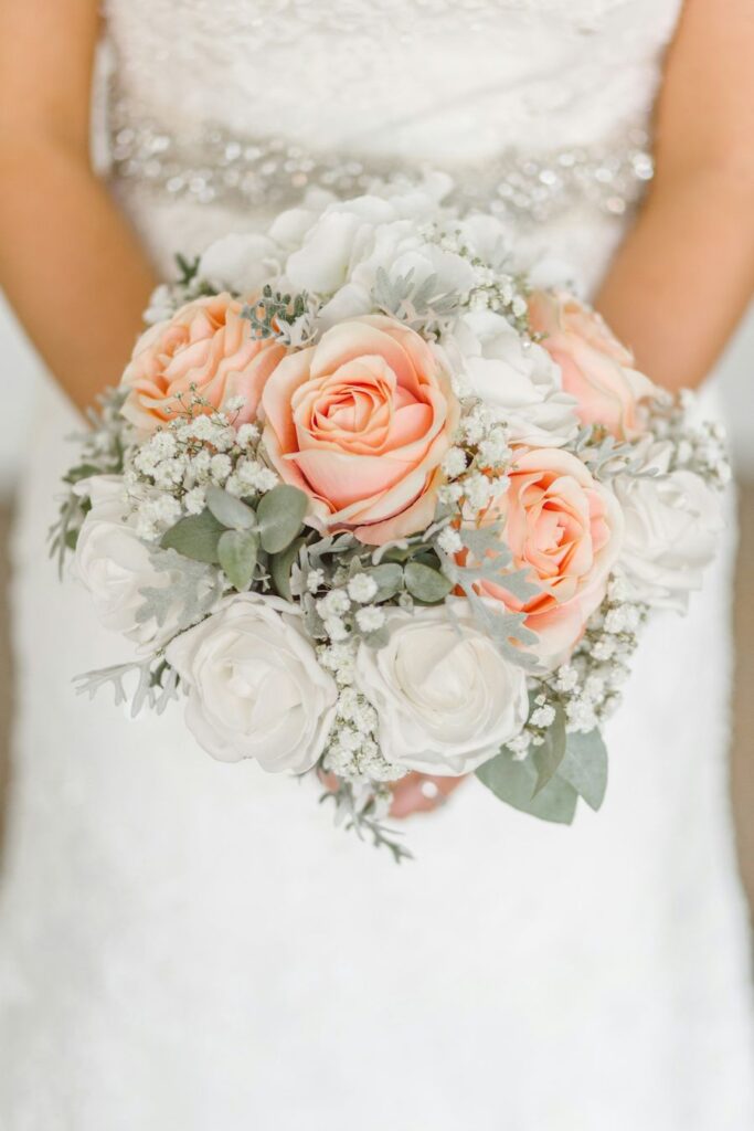 Bride holding a bouquet of peach roses and gypsophila