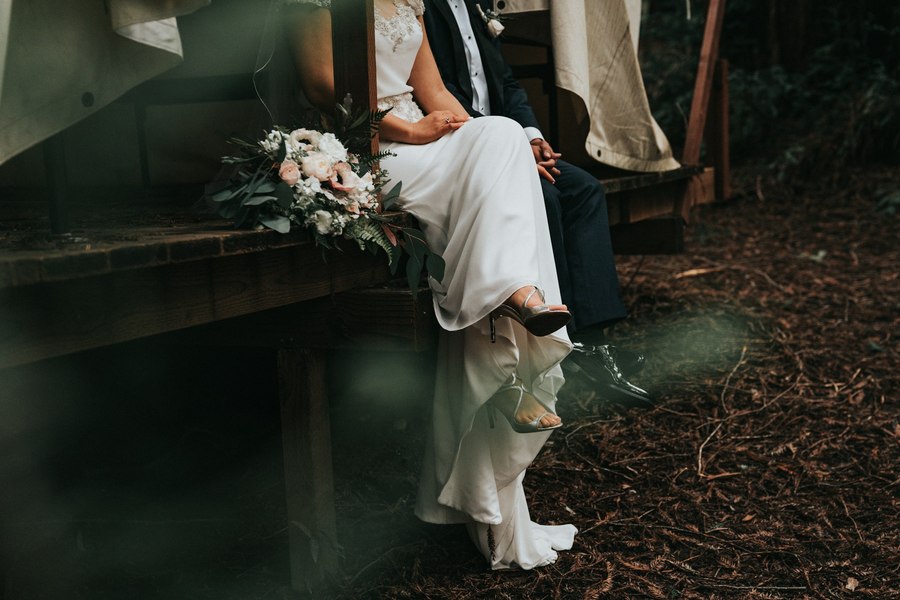 Bride and groom sitting together on wooden steps with a bouquet