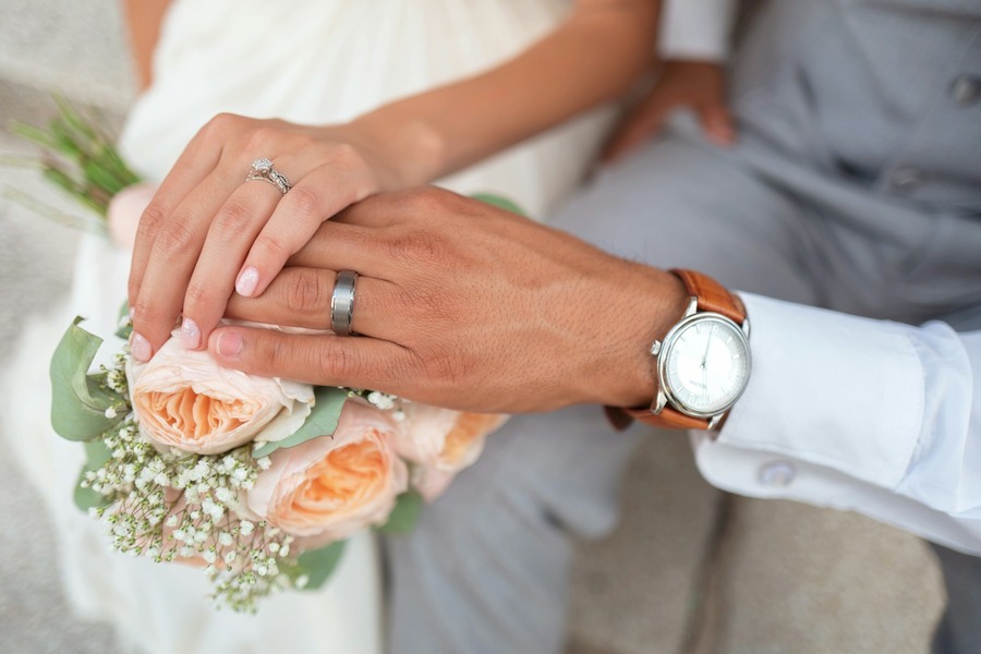 Newlyweds hands resting together over a bouquet, wedding rings showing