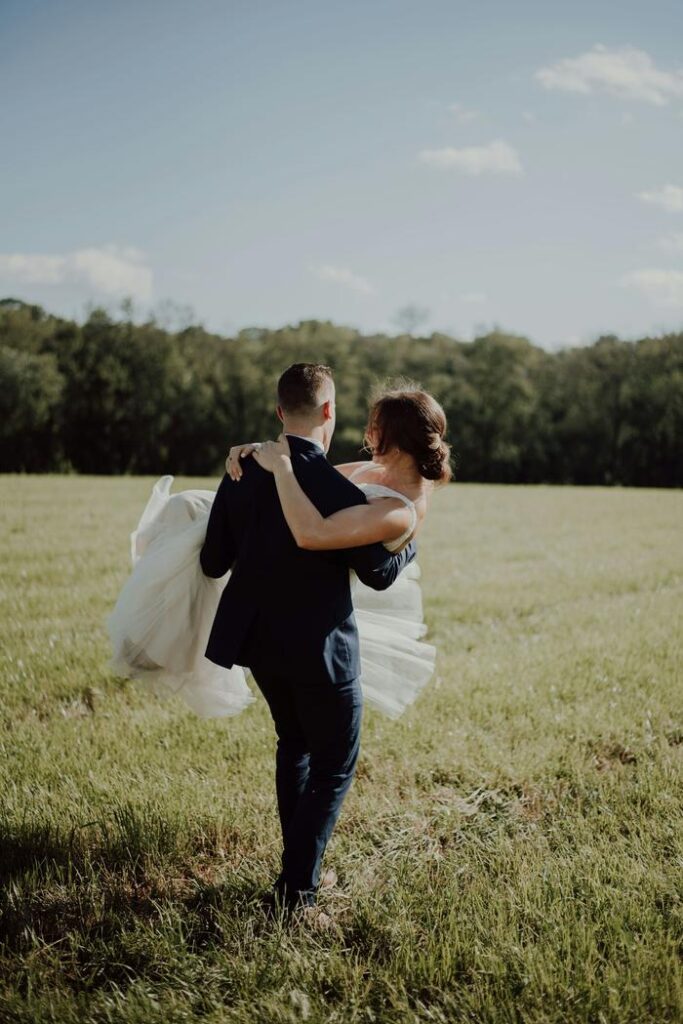 Groom carrying his bride across a meadow