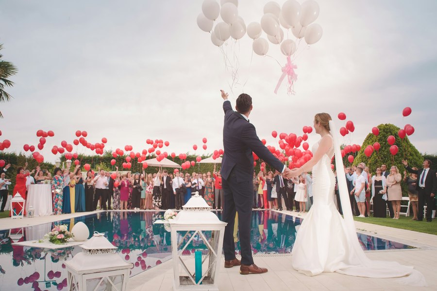 Couple releasing red and white balloons at a poolside ceremony